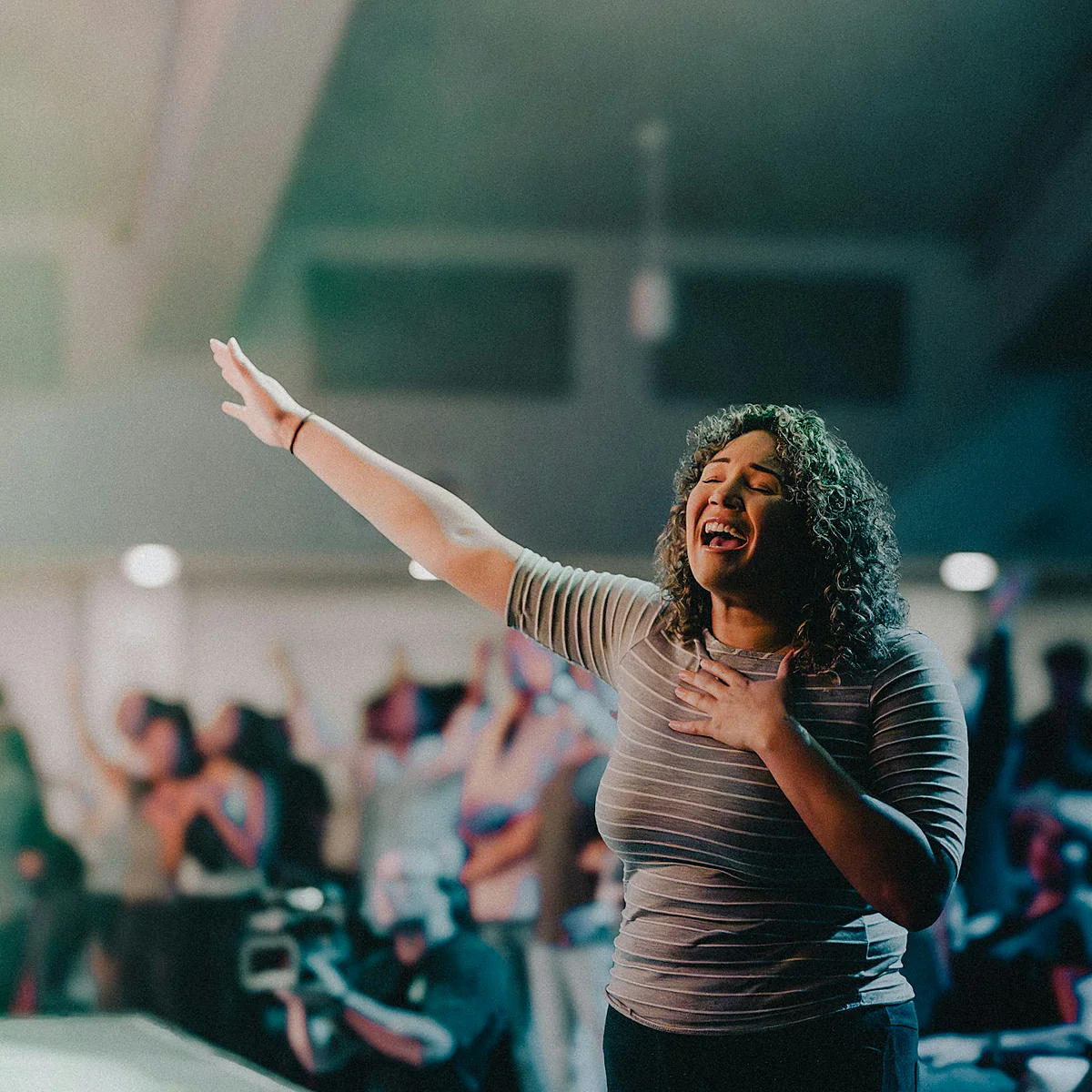 A worship leader singing with her hand raised during a church service.